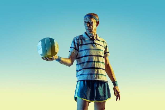 Senior man met sportkleding die volleybal speelt op gradiëntachtergrond, neonlicht.
