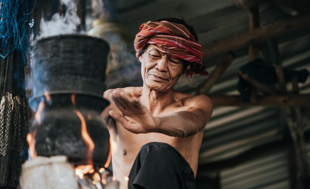 Senior man shirtless en tulband lendendoek gestoomde plakkerige rijst met een brandhoutkachel volgens het leven van de mensen op het platteland, kopieer ruimte, landelijke scène van het platteland in Thailand