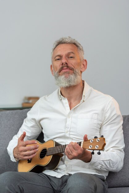 Senior man thuis die ukelele speelt op de bank