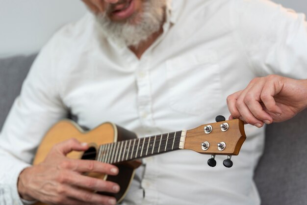 Senior man thuis die ukelele speelt op de bank