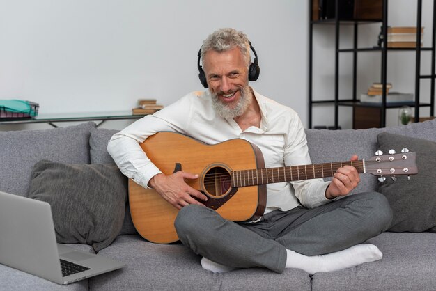 Senior man thuis op de bank met laptop om gitaarlessen te studeren