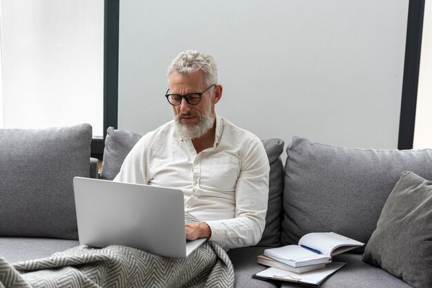 Senior man thuis studeren op de bank met behulp van laptop
