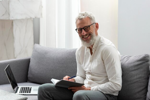 Senior man thuis studeren op laptop en aantekeningen maken