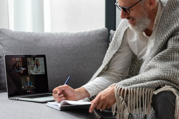 Senior man thuis studeren op laptop en aantekeningen maken