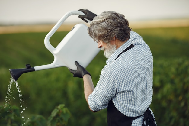 Gratis foto senior man zijn planten in zijn tuin met strooi water geven. man in een zwart schort.