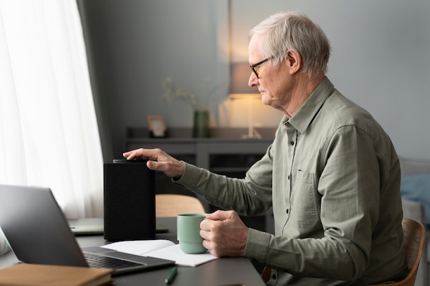 Senior man zit aan bureau en zet een luidspreker in de woonkamer aan