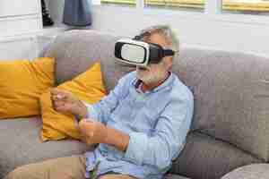 Gratis foto senior oude man ouderen genieten van het spelen van een spel met vr virtual reality-bril op de bank van de bank