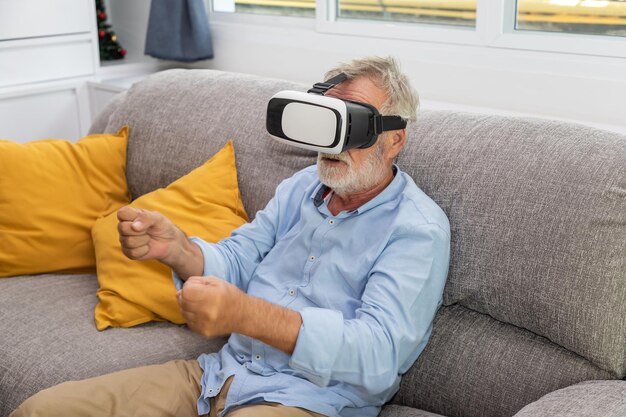 Senior oude man ouderen genieten van het spelen van een spel met VR Virtual Reality-bril op de bank van de bank