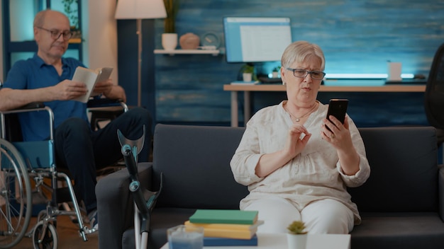 Senior persoon die smartphone vasthoudt om thuis te praten over teleconferentie. Gepensioneerde volwassene die online videoconferentie op mobiele telefoon gebruikt om een gesprek op afstand te voeren. Internet telecommunicatie