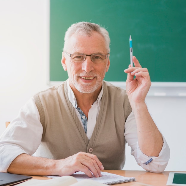 Senior professor met opgeheven hand met pen in de klas