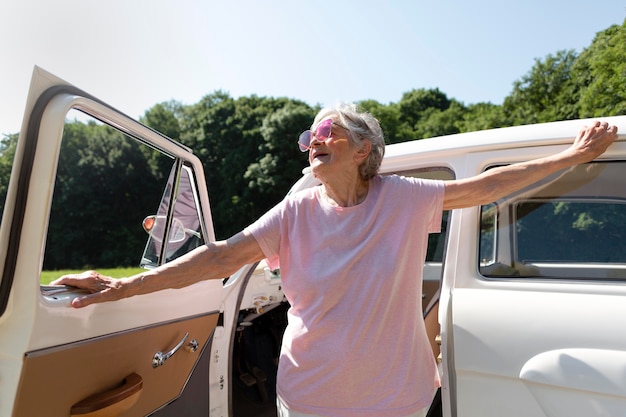 Senior reiziger met rode zonnebril naast haar auto