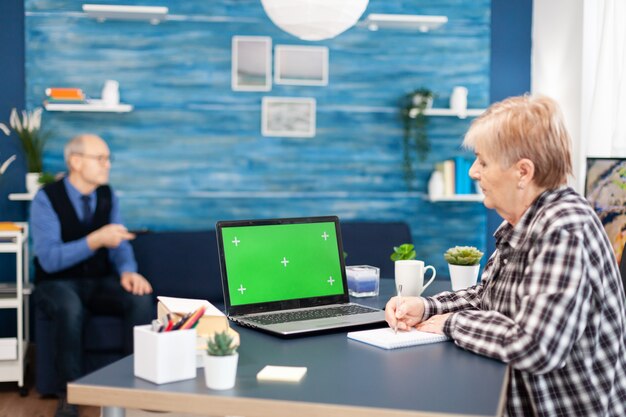 Senior vrouw die aantekeningen maakt op een notebook die naar een draagbare computer kijkt met beschikbare kopieerruimte