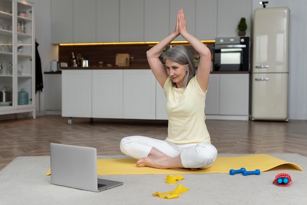 Senior vrouw die thuis fitnessles op laptop volgt