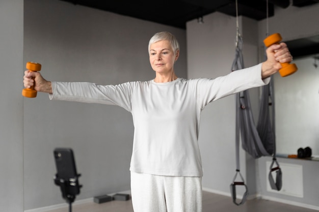 Gratis foto senior vrouw filmt zichzelf terwijl ze fitnessoefeningen doet in de sportschool