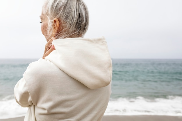 Senior vrouw in hoodie ontspannen op het strand