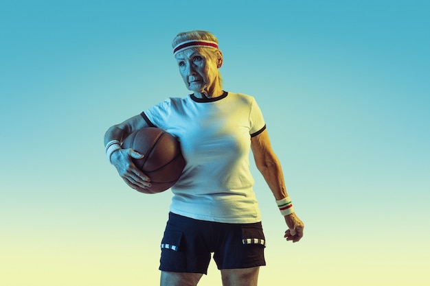 Gratis foto senior vrouw in sportwear basketbal spelen op verloop achtergrond, neon licht. vrouwelijk model in uitstekende conditie blijft actief. concept van sport, activiteit, beweging, welzijn, vertrouwen. copyspace.