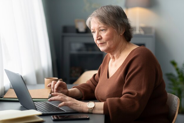 Senior vrouw met behulp van laptop zit aan bureau in woonkamer