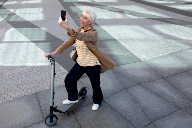 Gratis foto senior vrouw met een elektrische scooter in de stad die een selfie maakt