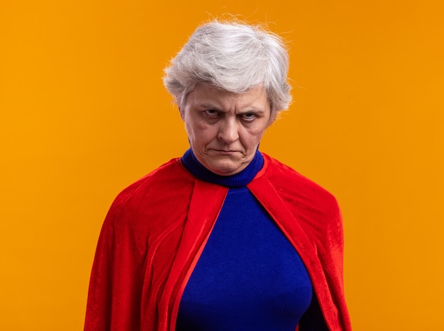 Senior vrouw superheld dragen rode cape camera kijken met boos gezicht fronsen
