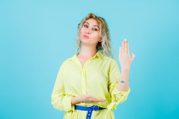 Gratis foto serieus blonde vrouw toont haar hand naar camera op blauwe achtergrond