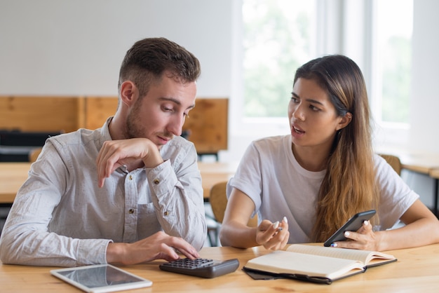 Serieuze studenten bespreken huiswerk en het gebruik van digitale apparaten