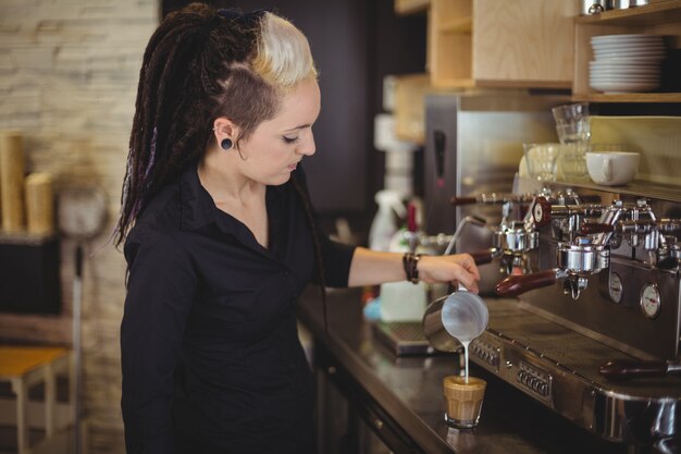 Serveerster die melk gieten in koffiekop bij teller