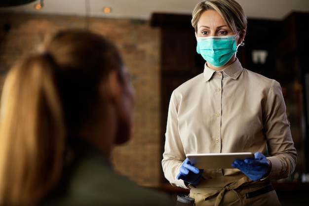 Serveerster met een gezichtsmasker die de bestelling van de klant opneemt op een digitale tablet in een café