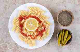 Gratis foto serveren van macaroni met kleine kommen zwarte peper en ingemaakte pepers op marmeren oppervlak.