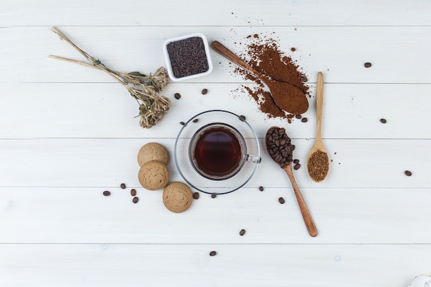 Set van gemalen koffie, koffiebonen, gedroogde kruiden, koekjes en koffie in een kopje op een houten achtergrond. bovenaanzicht.