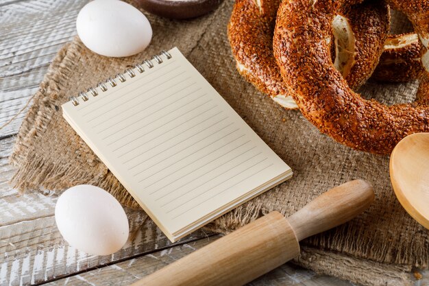 Set van Kladblok, eieren, deegroller en Turkse bagel op een zak doek en houten oppervlak. hoge hoekmening.