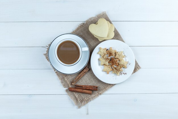 Set van koekjes, kaneelstokjes en koffie in een kopje op houten en stuk zak achtergrond. bovenaanzicht.