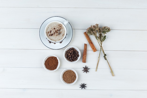 Set van koffiebonen, gemalen koffie, specerijen, koekjes, gedroogde kruiden en koffie in een kopje op een houten achtergrond. bovenaanzicht.