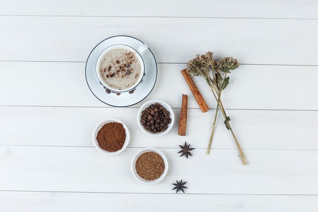 Set van koffiebonen, gemalen koffie, specerijen, koekjes, gedroogde kruiden en koffie in een kopje op een houten achtergrond. bovenaanzicht.