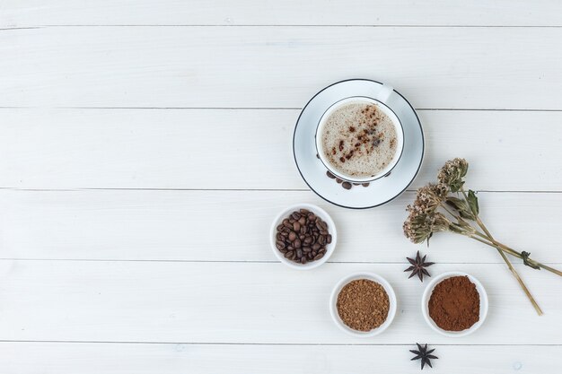 Set van koffiebonen, gemalen koffie, specerijen, koekjes, gedroogde kruiden en koffie in een kopje op een houten achtergrond. bovenaanzicht.