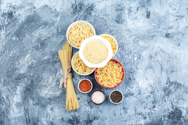 Set van kruiden en diverse pasta in kommen op een grijze gips achtergrond. bovenaanzicht.