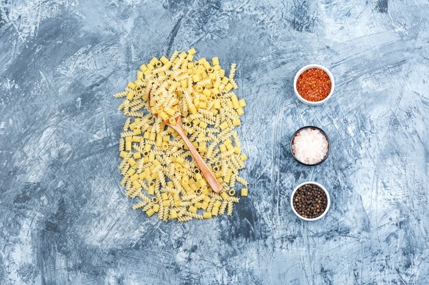 Set van kruiden en verspreide pasta in een houten lepel op een grungy gips achtergrond. plat leggen.