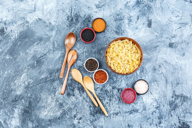 Set van kruiden, houten lepels en rauwe pasta in een kom op een grijze gips achtergrond. bovenaanzicht.