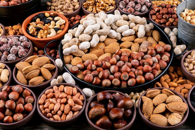 Set van pecannoten, pistachenoten, amandel, pinda, cashewnoten, pijnboompitten en diverse noten en gedroogde vruchten in verschillende kommen. zijaanzicht.