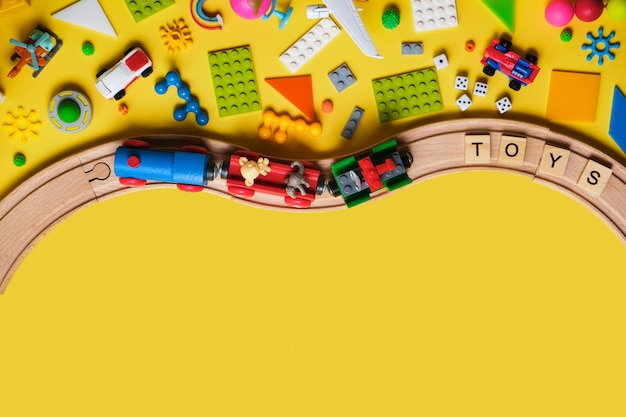 Set van verschillende kinderspeelgoed, houten spoorweg, trein, constructeur op een gele achtergrond met kopie ruimte voor tekst. bovenaanzicht, plat gelegd.