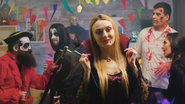Sexy blonde in tovenares kostuum dansen op een halloween-feest. Groep mensen die halloween vieren in een ingerichte kamer.
