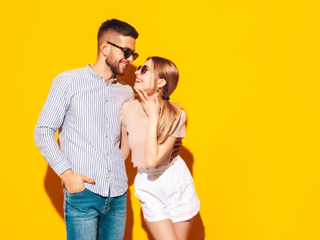 Sexy lachende mooie vrouw en haar knappe vriendje Gelukkige vrolijke familie met tedere momenten in de buurt van gele muur in studioPure vrolijke modellen knuffelen omhelzen elkaar in zonnebril