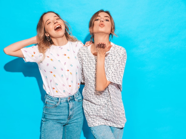 Sexy onbezorgde vrouwen die dichtbij blauwe muur stellen. Positieve modellen hebben plezier en tonen grappige grimas