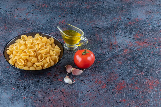 Shell ongekookte pasta in een glazen kom met verse rode tomaat en knoflook.