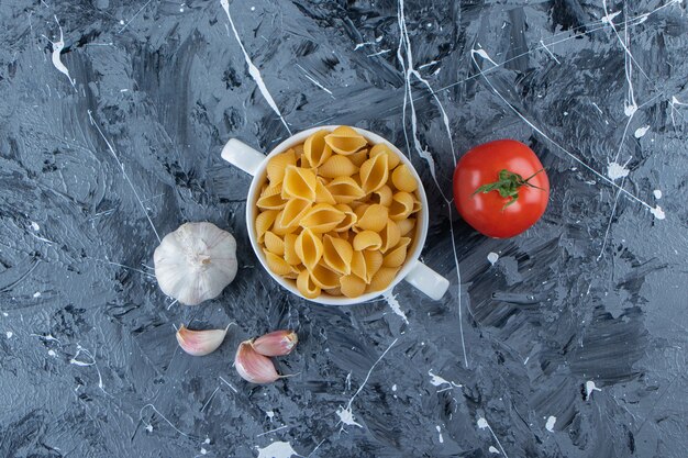 Shell ongekookte pasta in een kom met verse rode tomaten en knoflook.