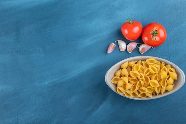 Shell ongekookte pasta in een kom met verse rode tomaten en knoflook.