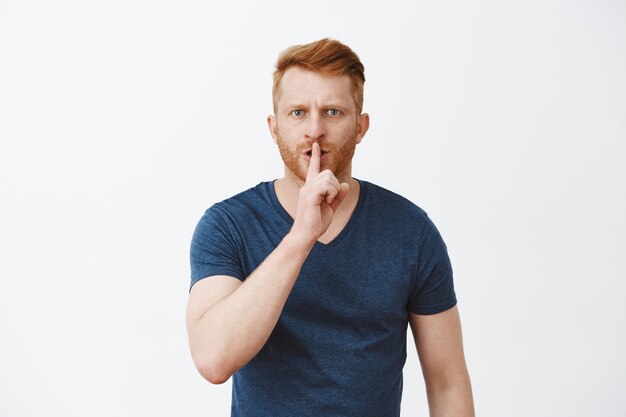 Shh ik heb concentratie nodig. Portret van intens ernstig ogende ontevreden roodharige man met borstelharen, die een stil gebaar toont met wijsvinger over de mond, fronsend, veeleisend zwijgen of geheim houden