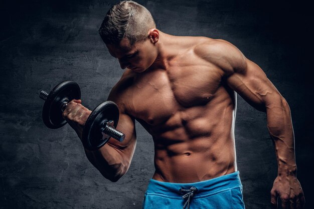 Shirtless atletische man doet biceps trainingen met een halter op grijze vignet achtergrond.