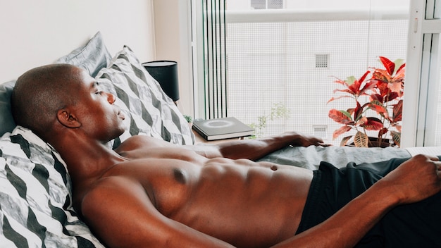 Gratis foto shirtless fit afrikaanse jongeman ontspannen op bed