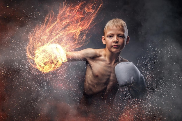 Shirtless jonge bokser met blond haar die bokshandschoenen draagt, toont een bokshaak. Geïsoleerd op een donkere achtergrond.