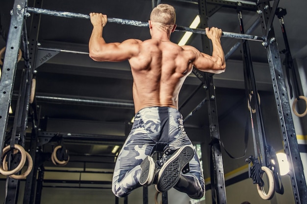 Shirtless man optrekken op rekstok in een sportschool.